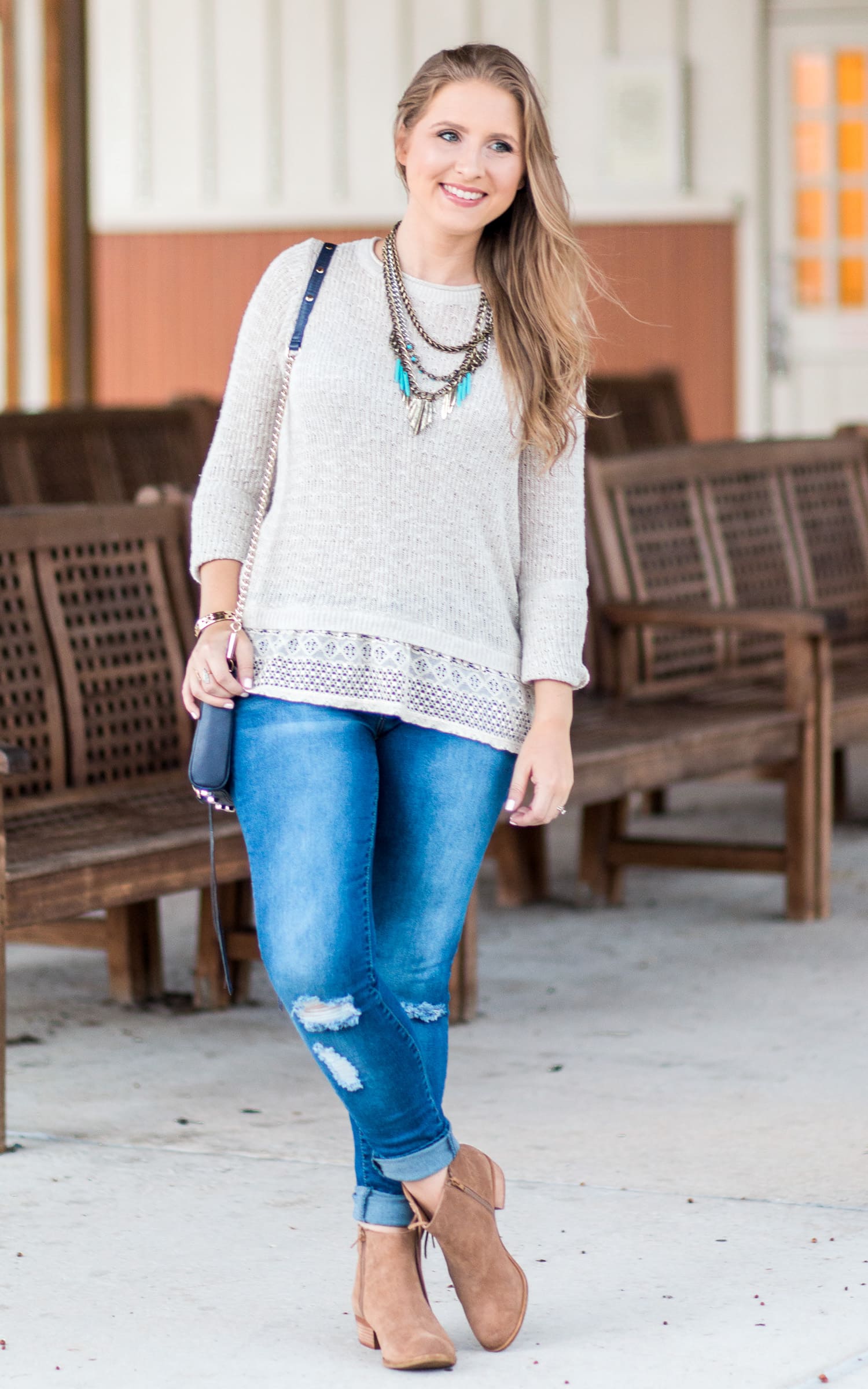 Cute fall outfit idea featuring a cream sweater with lace ruffle, destroyed denim jeans, navy crossbody bag, antiqued gold and turquoise statement necklace, and Lucky Brand Beeliner fringe booties styled by blogger Ashley Brooke Nicholas.