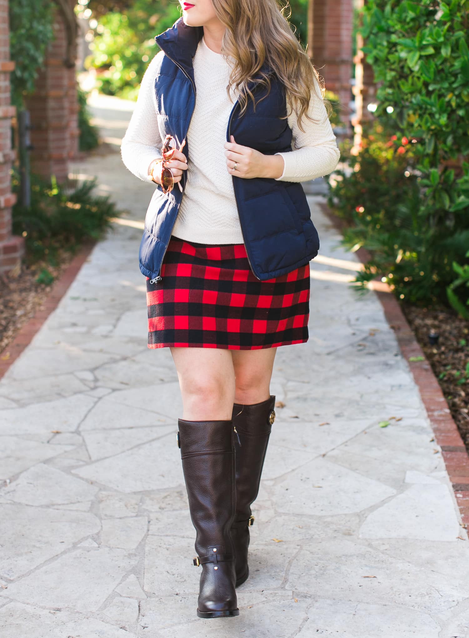 A cozy fall outfit + the best Gap and Old Navy Black Friday Deals +  get $20 back with any $50 purchase at Gap Inc with your Marriott Rewards Premier Card. Preppy fall outfit idea featuring Old Navy navy puffer vest, cream sweater, red plaid skirt, Tory Burch boots, Foster Grant sunglasses, and Clinique Cherry Pop lipstick styled by Florida fashion blogger Ashley Brooke Nicholas